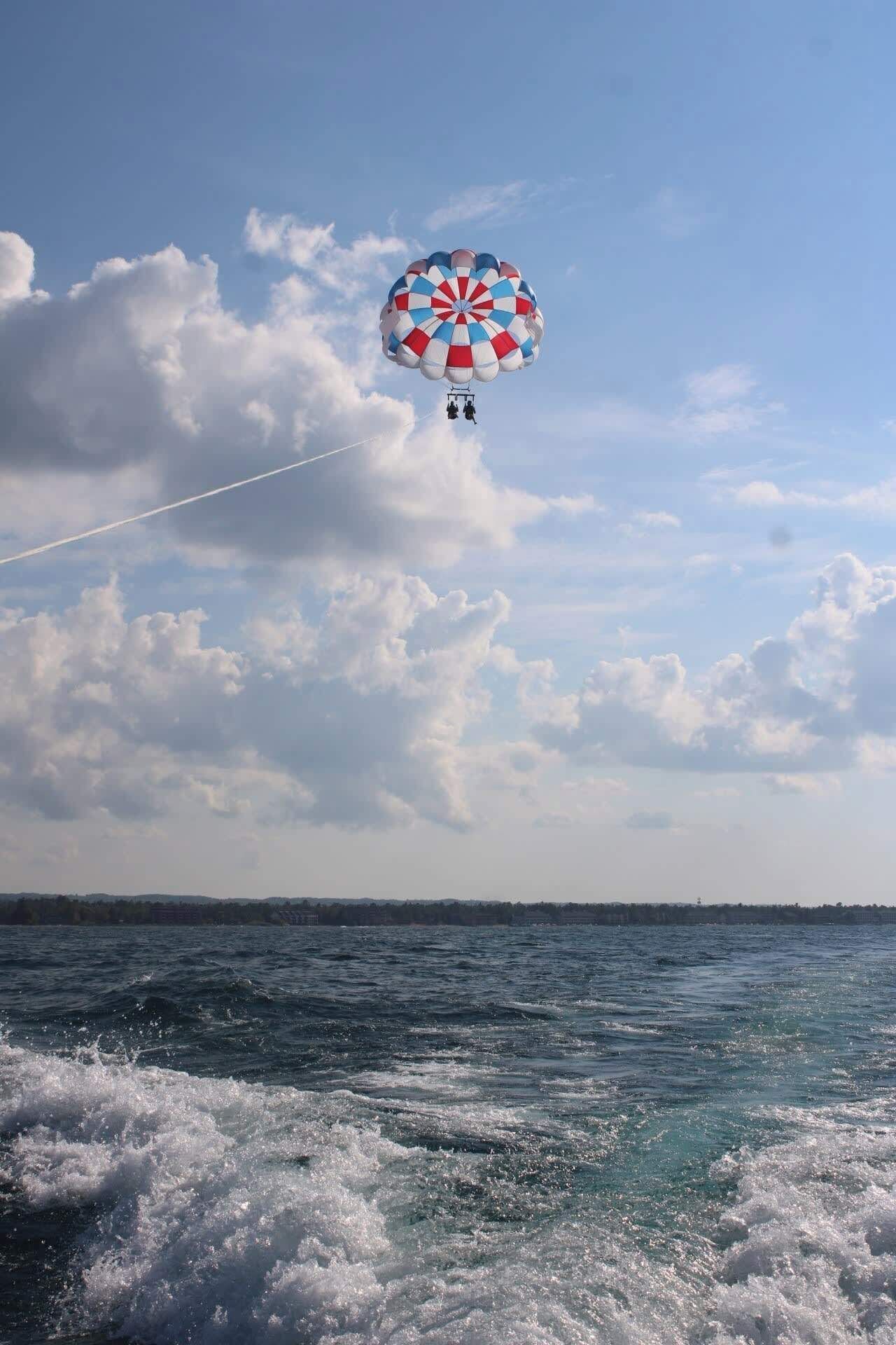 Une personne fait du parachute ascensionnel au-dessus de l’eau, sous un ciel dégagé.