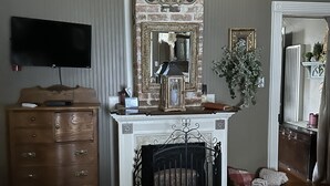 Een woonkamer met een open haard, een aan de muur bevestigde televisie, een houten dressoir en een spiegel boven de open haard.