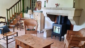 Un salon chaleureux avec une cheminée, des meubles en osier et un escalier menant à l’étage.
