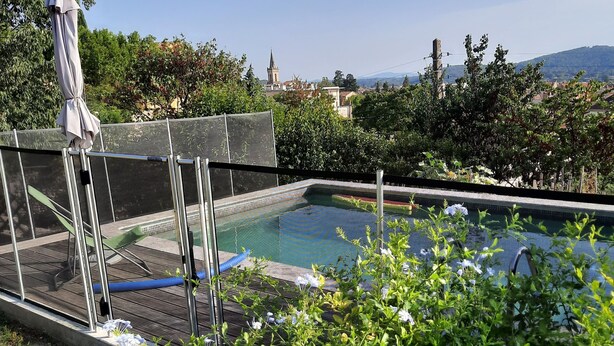 Une piscine dotée d ’un espace couvert, entourée de verdure et offrant une vue sur des bâtiments éloignés.