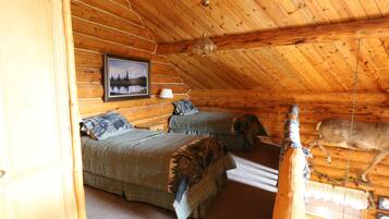 A log cabin bedroom with two beds, a hanging light fixture, and a deer in the ceiling.