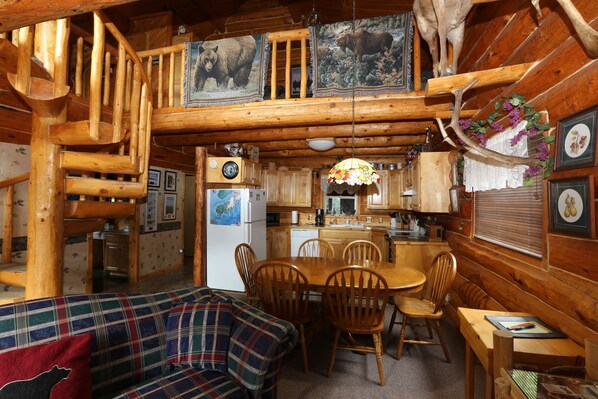 A cabin interior with a dining area, wooden staircase, and a cozy living space.