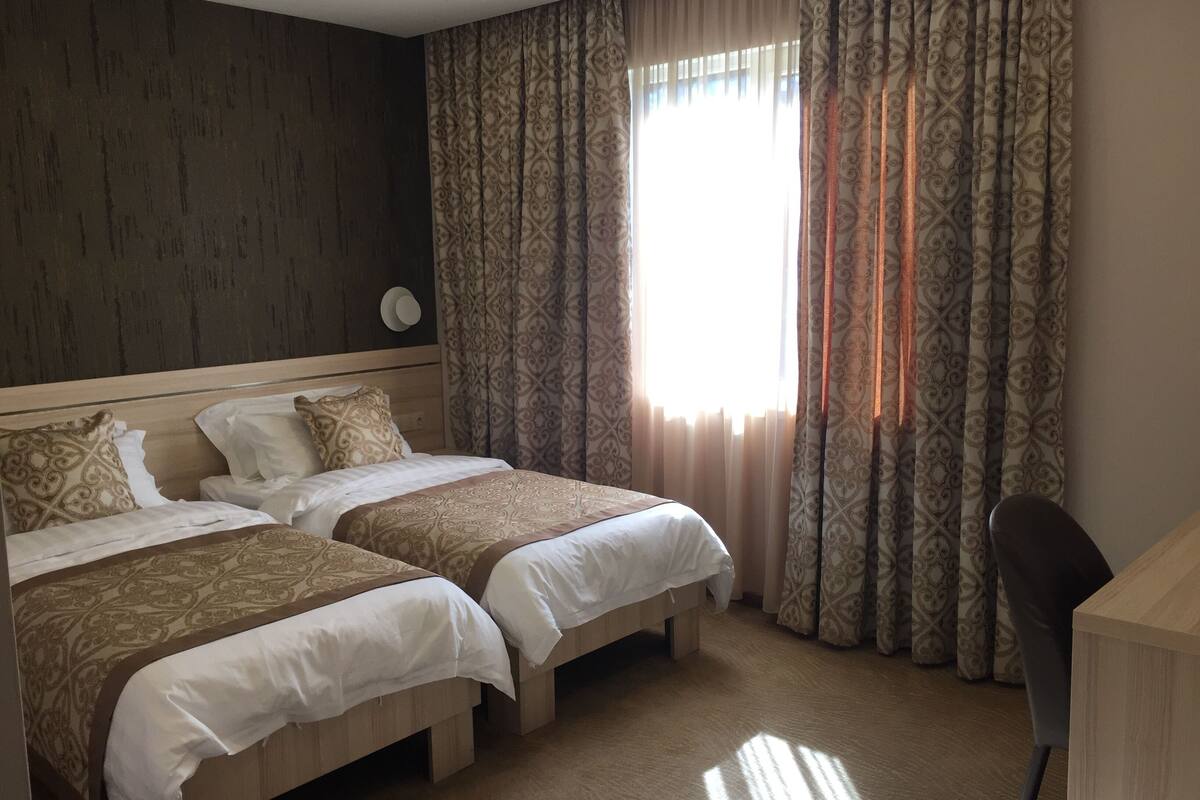 Una habitación de hotel con dos camas, un escritorio y un ventanal con cortinas estampadas.