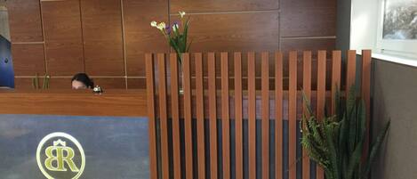 A reception desk with a wooden slat partition, a potted plant, and a framed picture on the wall.