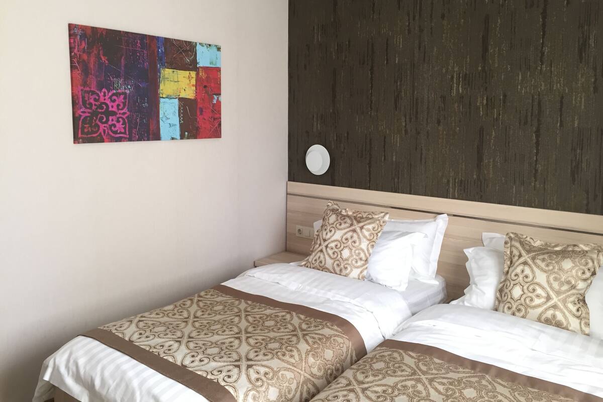 Habitación de hotel con cama, cabecera decorativa, obra de arte colgada en la pared y un reloj de pared redondo.