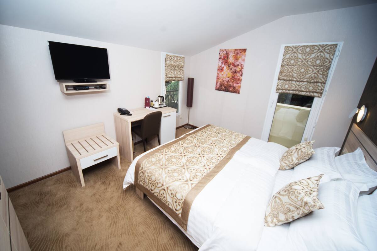 Una habitación de hotel con cama, escritorio, silla, televisor y ventana con persianas.