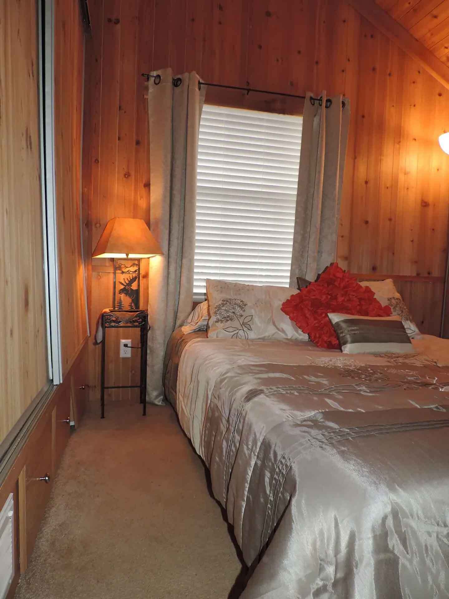 A cozy bedroom with a bed, a nightstand with a lamp, and a window with curtains.