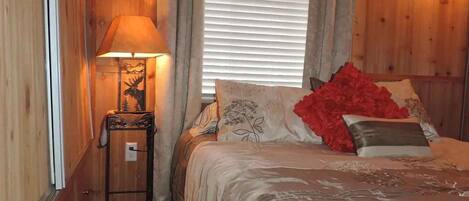A cozy bedroom with a bed, a nightstand with a lamp, and a window with curtains.