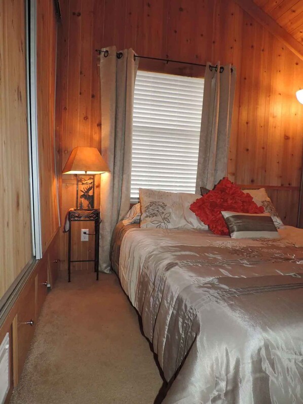 A cozy bedroom with a bed, a nightstand with a lamp, and a window with curtains.