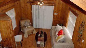 A cozy attic room with a wooden ceiling, a ceiling fan, a sofa, a small table, and a window with blinds. - Wildflowers Cabin @ HomeAway Ranch (Boerne)