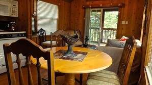 A cozy cabin interior with a wooden dining table, chairs, a sofa, and a kitchen area with a stove and refrigerator. - Wildflowers Cabin @ HomeAway Ranch (Boerne)