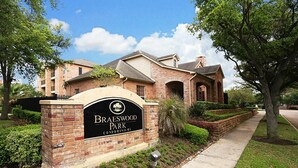 Une enseigne indiquant l’entrée de la résidence Braeswood Park, avec un bâtiment en briques et un jardin aménagé.