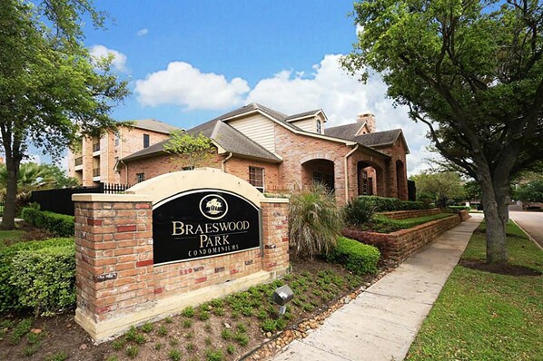 Letrero de Braeswood Park Condominiums, con un edificio de ladrillo y jardín ajardinado.