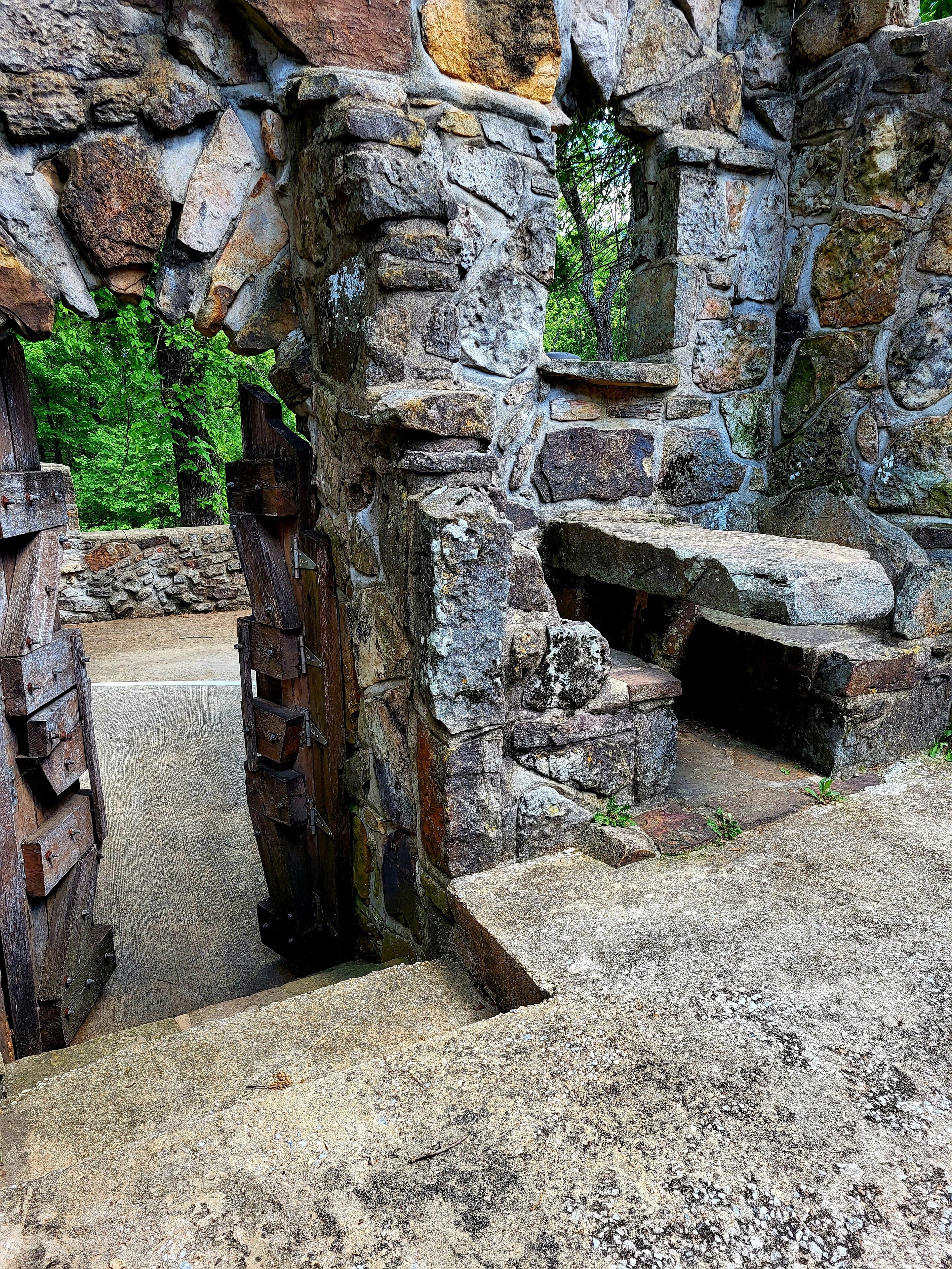 A stone structure with a rustic, historical appearance, featuring a stone bench and a wooden door.