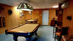 Une table de billard dans une pièce aux murs en bois, une table à manger avec des chaises et un luminaire au plafond.