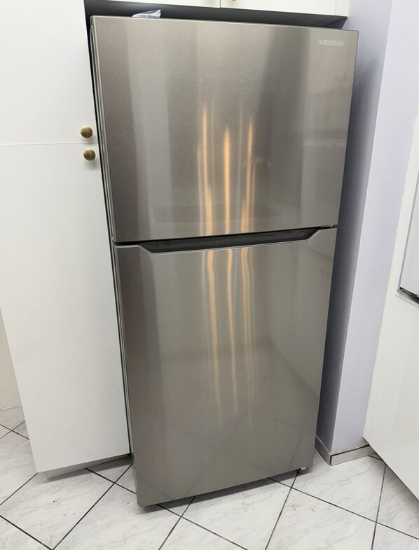 Un réfrigérateur en acier inoxydable à double porte, installé dans une cuisine dotée de meubles blancs et d’un revêtement de sol carrelé.