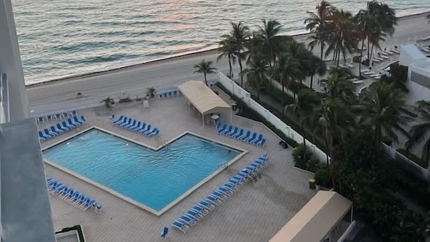 Zwembad van een resort met uitzicht op de zonsondergang boven de oceaan, met palmbomen en ligbedden.