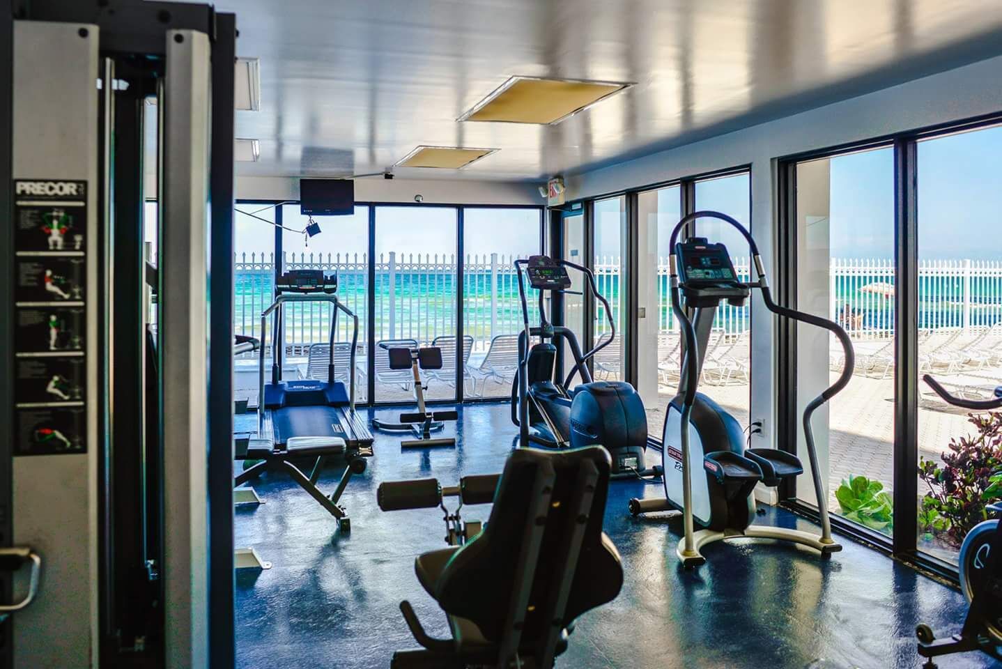 Une salle de sport équipée de matériel d’exercice et dotée de grandes fenêtres donnant sur une plage.