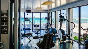 Een fitnessruimte met trainingsapparatuur en grote ramen met uitzicht op een strand.