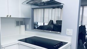 Een moderne keuken met witte kasten, een zwart inductiefornuis en een roestvrijstalen afzuigkap.