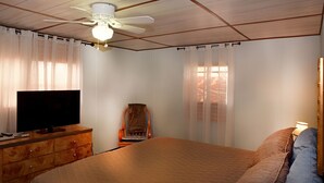 A bedroom with a bed, a wooden dresser, a television, and a ceiling fan.
