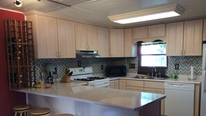 A kitchen with light wooden cabinets, a central island with stools, a stove, microwave, and dishwasher.