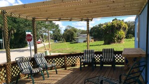 A covered outdoor deck with wooden flooring, striped outdoor furniture, and a view of a street with a stop sign.
