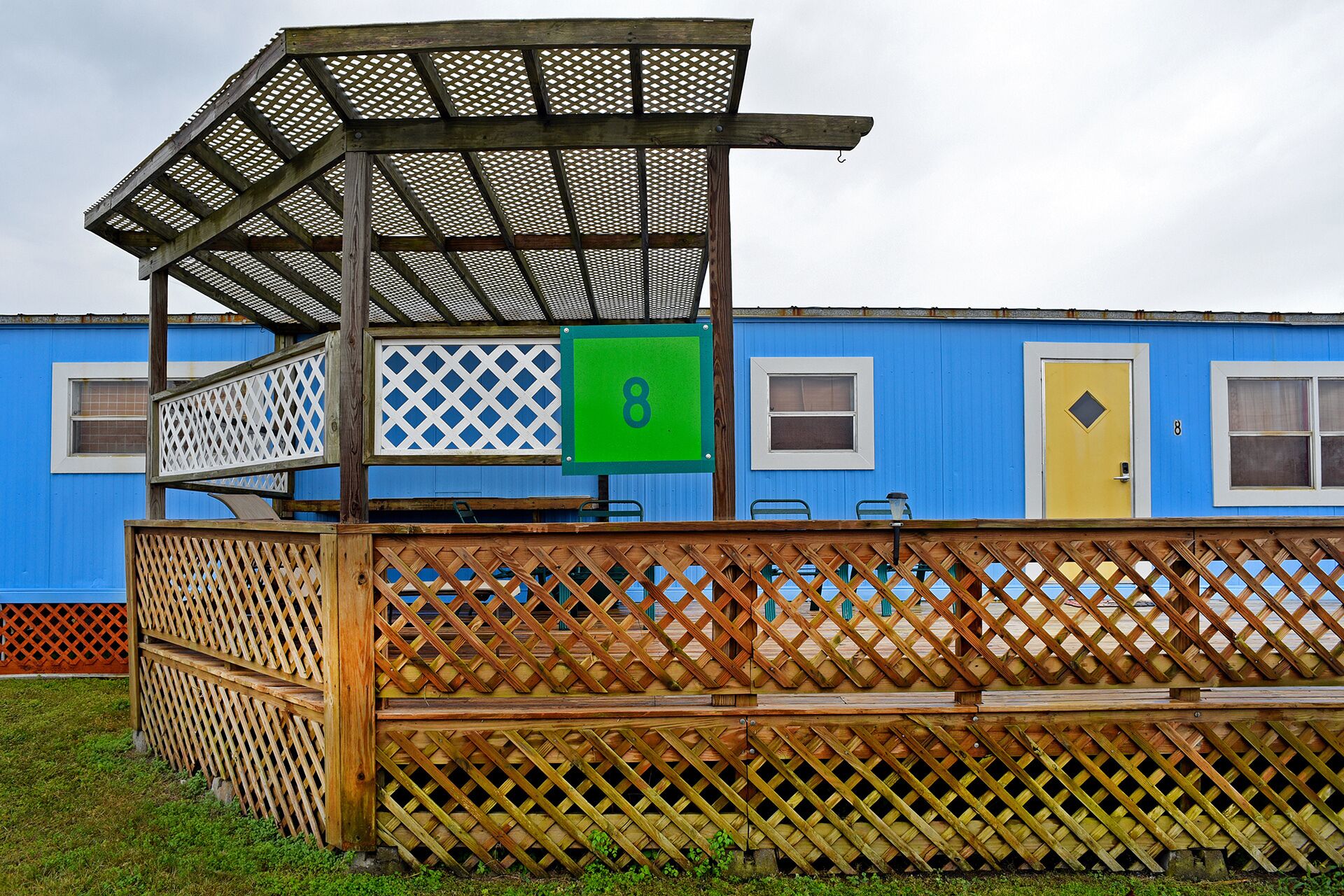 Un bâtiment bleu avec une porte jaune, une enseigne verte portant le numéro 8 et une clôture en bois.