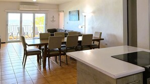 Ein Essbereich mit Tisch und Stühlen, eine Kücheninsel und Meerblick durch eine Schiebetür.