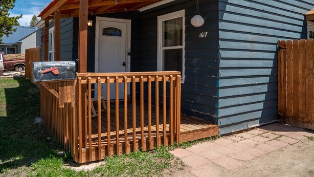 Ein kleines Haus mit einer Holzdiele, einem Briefkasten und der Hausnummer 1617 an der Tür.