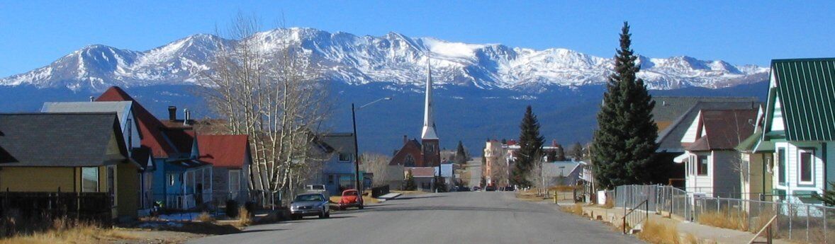 Une rue bordée d’immeubles et d’une église, avec des montagnes enneigées en arrière-plan.