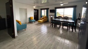 A spacious living area with a dining table and chairs, a sofa, and a TV mounted on the wall.