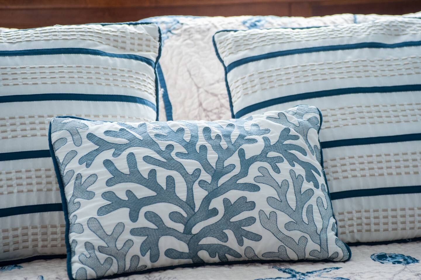 Un letto con una coperta a righe bianche e blu e un cuscino a motivi corallo.