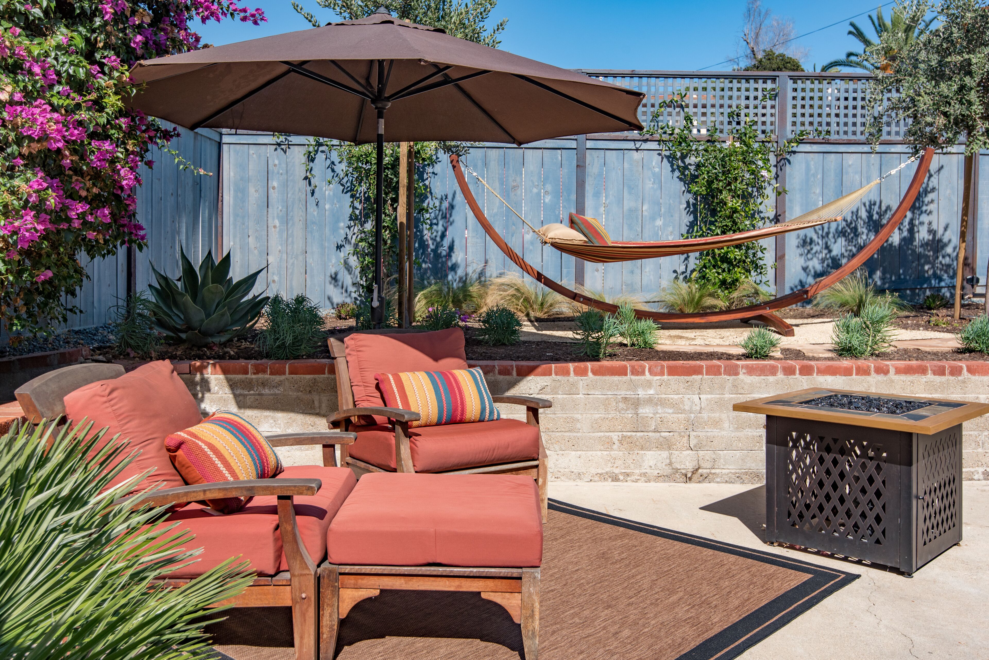 A patio with a hammock, two cushioned chairs, a table, and an umbrella.