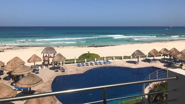 Ein Pool in einem Resort mit Reetdachschirmen, Liegestühlen und Blick auf Strand und Meer.
