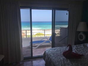 Een kamer met een bed, een rode zwaan decoratie, uitzicht op het strand en de oceaan door een schuifdeur, en een stoel buiten.