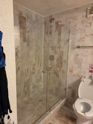 Et badeværelse med et glasafskærmet brusebad, toilet og et håndklædestativ.