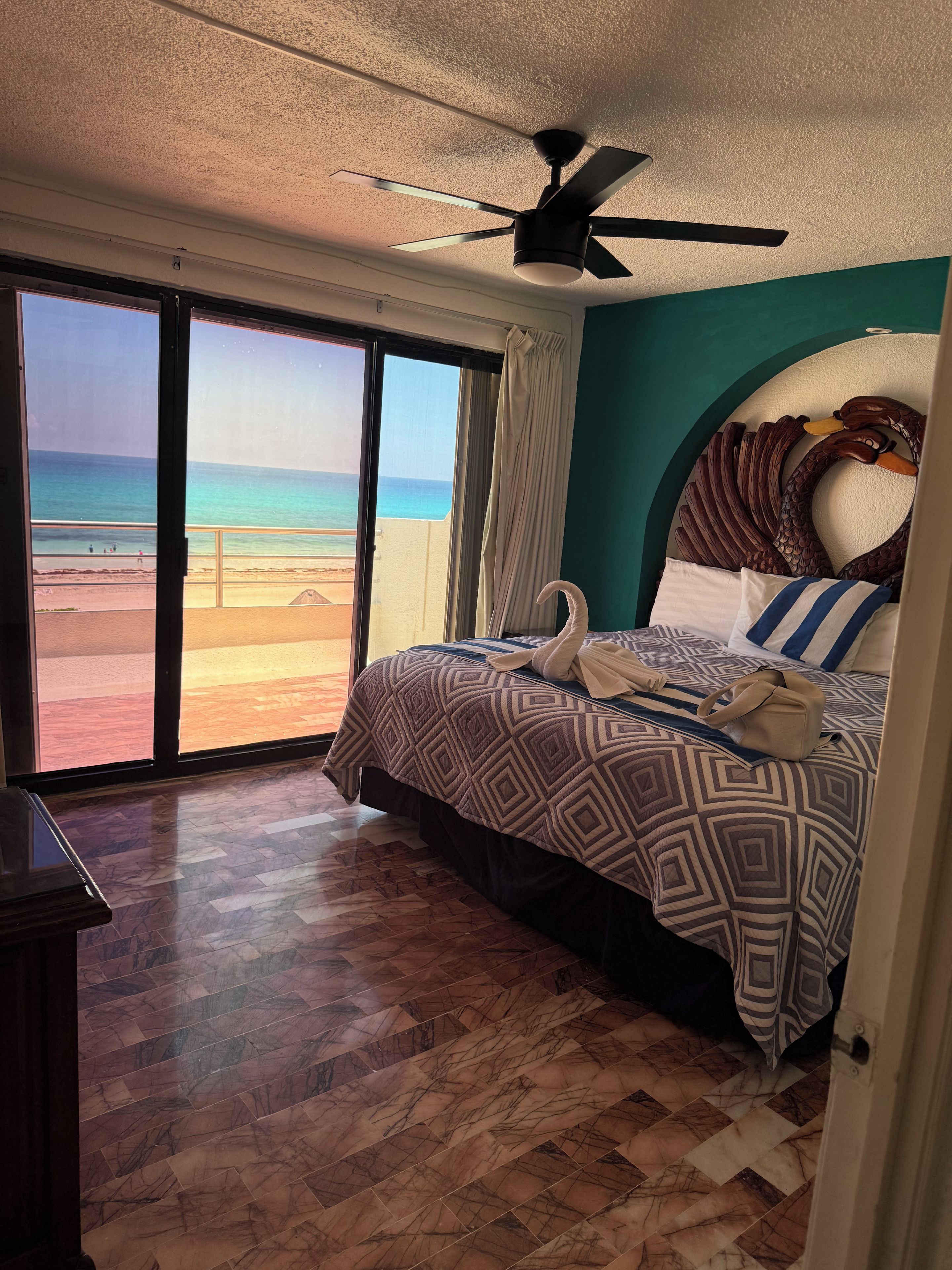 Une chambre avec un lit, un ventilateur de plafond, une vue sur la plage et un plancher en bois.