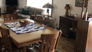 Zona pranzo con tavolo in legno, sedie, un lampadario e una televisione sullo sfondo.