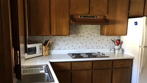 Una cucina con mobili in legno, un piano di lavoro bianco, un forno a microonde, un fornello e un frigorifero.