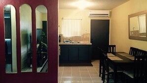 Un comedor con mesa y sillas, una cocina con lavaplatos y mostrador, y una puerta con espejo.