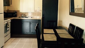 Cocina compacta con microondas, pileta y estufa, zona de comedor con mesa y sillas, y equipo de aire acondicionado sobre la puerta.