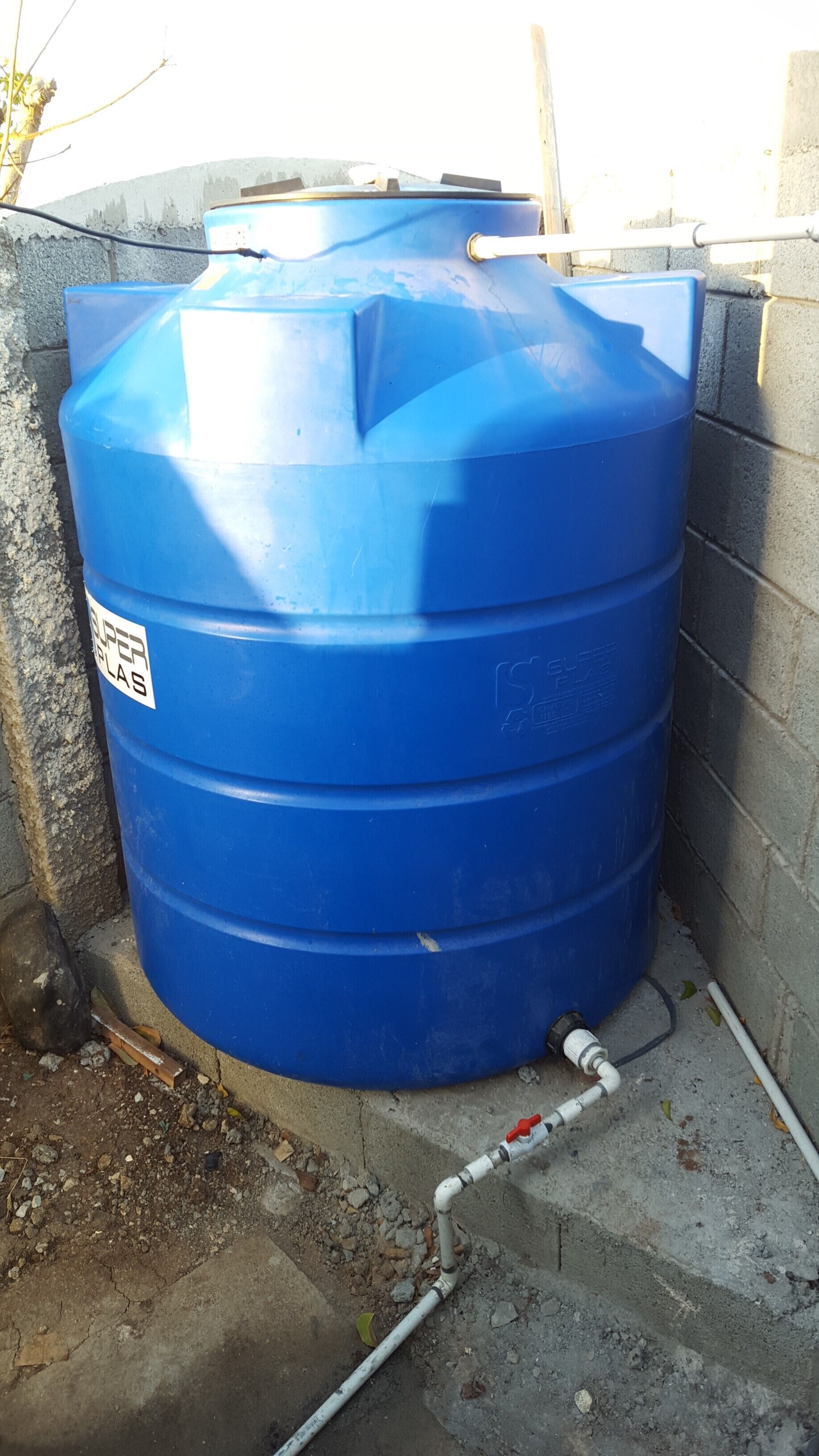 Un tanque grande azul para almacenamiento de agua con una etiqueta blanca, conectado a un sistema de tuberías blancas.