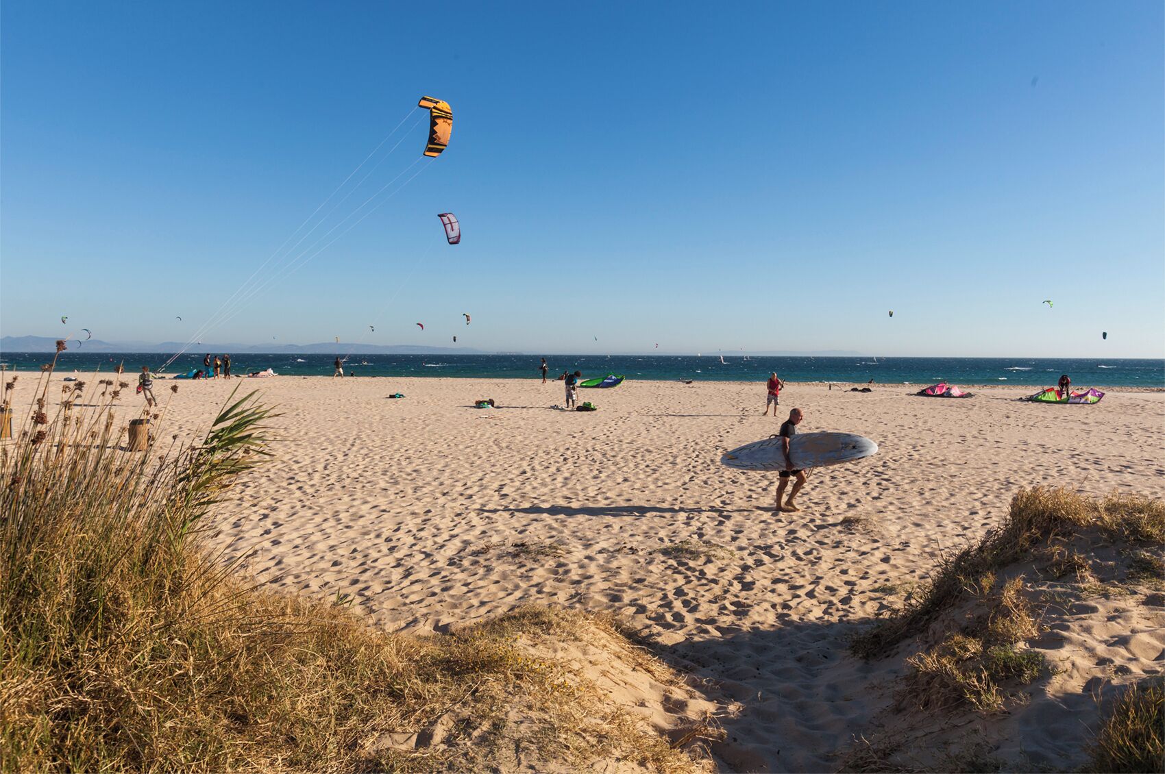 En sandstrand med folk, drakar och en klar himmel.