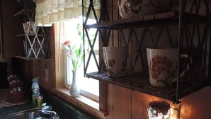A kitchen with wooden cabinets, a window with a view, a sink, and a hanging shelf with decorative items. - Hansel & Gretel Charming Cabin @ HomeAway Ranch & NoahSanctuary - Pet friendly! (Boerne)