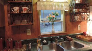 A kitchen with wooden walls, a window with a view, and shelves with kitchenware. - Hansel & Gretel Charming Cabin @ HomeAway Ranch & NoahSanctuary - Pet friendly! (Boerne)