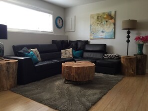 A modern living room with a black leather sofa, a round wooden coffee table, and a grey shag rug.