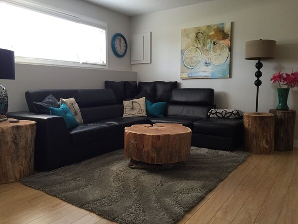 Uma sala de estar moderna com um sofá de couro preto, uma mesa de centro redonda de madeira e um tapete felpudo cinza.