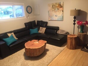 Uma sala de estar com um sofá de couro preto, uma mesa de centro redonda de madeira e um quadro de uma bicicleta na parede.