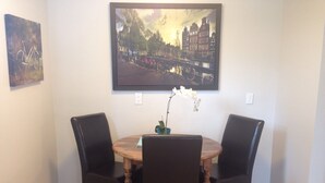 Un coin repas avec une table ronde en bois, quatre chaises noires et un tableau encadré représentant une vue de la ville, accroché au-dessus.